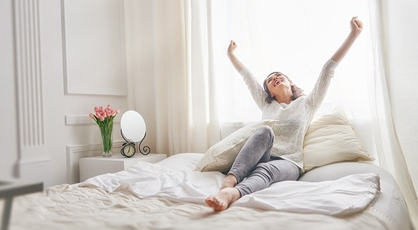Happy young woman enjoying sunny morning on the bed